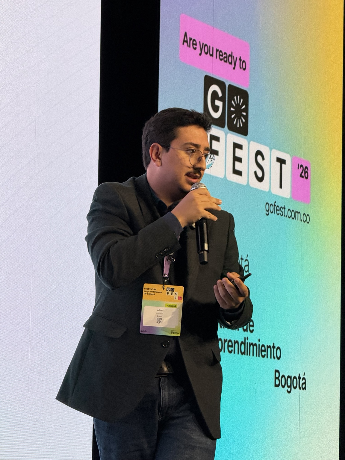 Julián Caicedo habla con micrófono en mano durante el Pitch Competition, con la pantalla de GOFest 2026 de fondo.